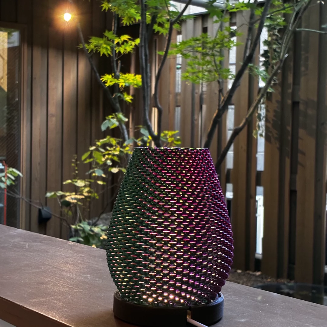 Iridescent NITE Weave lamp lit under a wooden pergola with maple foliage